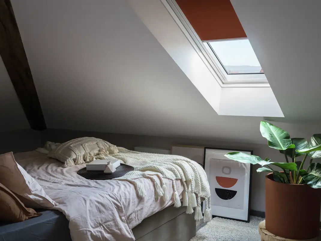 Attic bedroom with sloped ceiling and VELUX roof window, cozy decor.