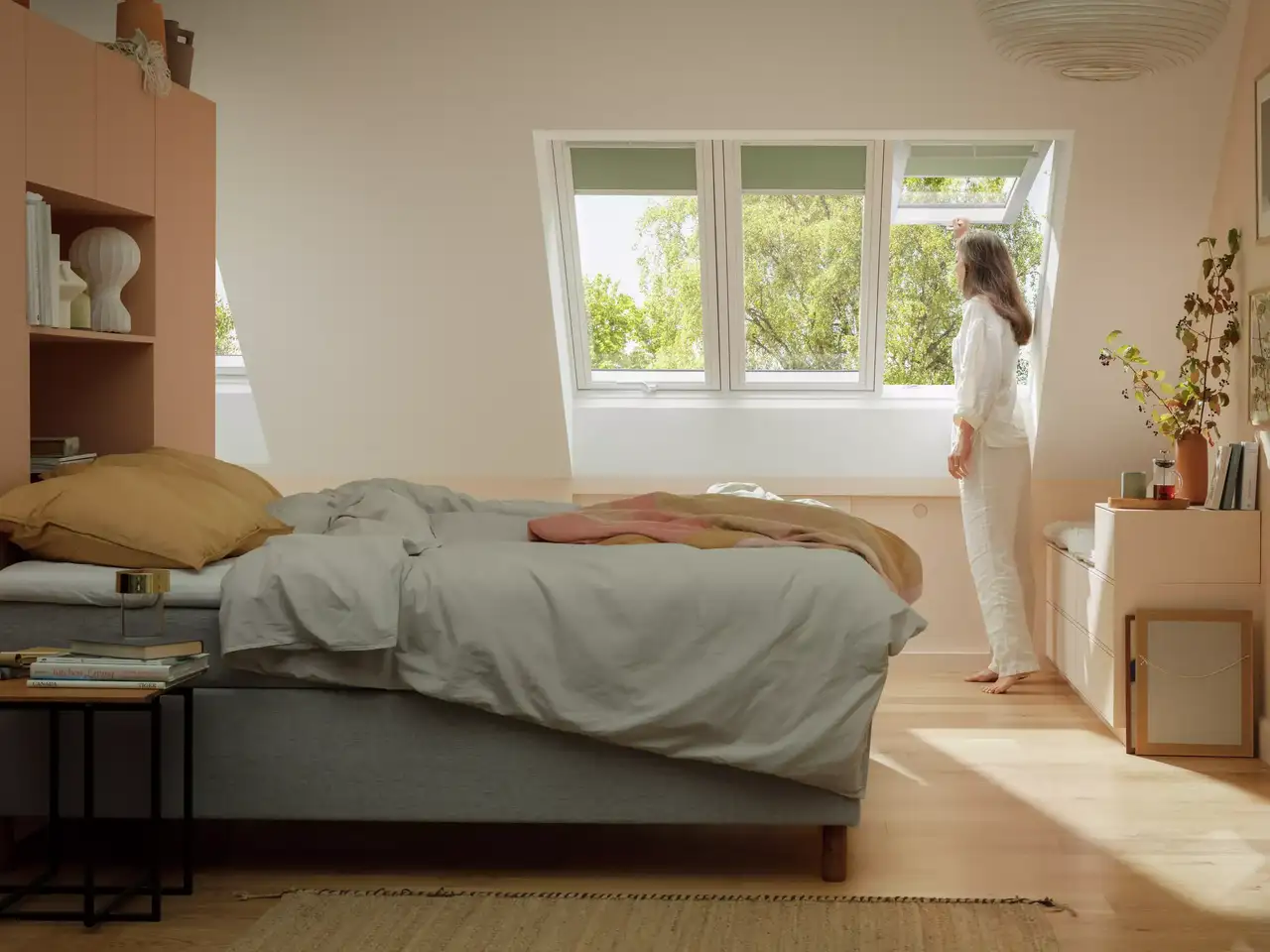 Attic bedroom with sloped ceiling and VELUX window, woman enjoying view.