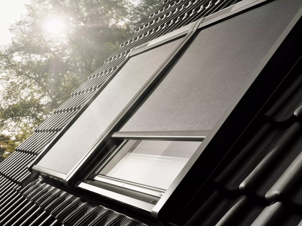 VELUX roof window with sunshade on a steeply pitched black tile roof.
