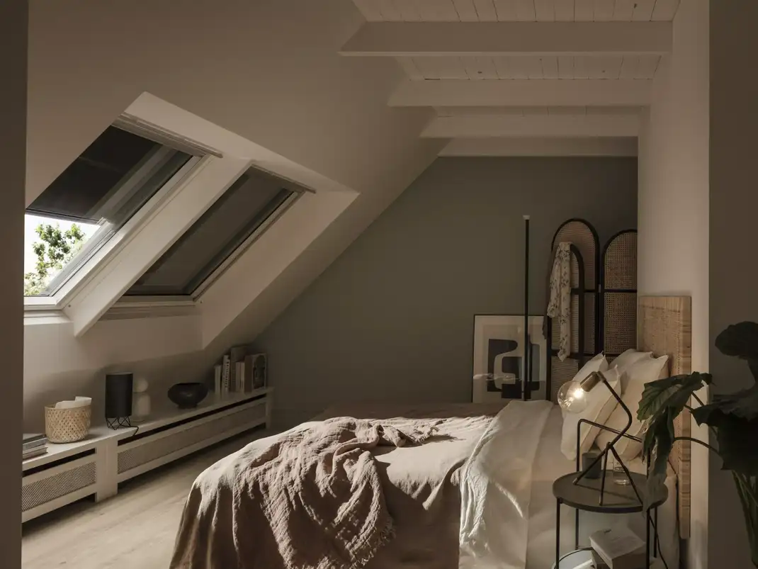Attic bedroom with sloped ceiling and VELUX roof window, cozy decor.