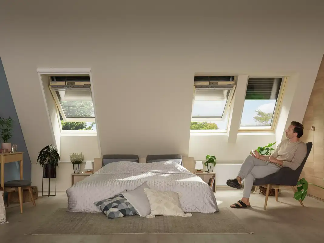 Attic bedroom with sloped ceiling and open VELUX roof windows, natural light.